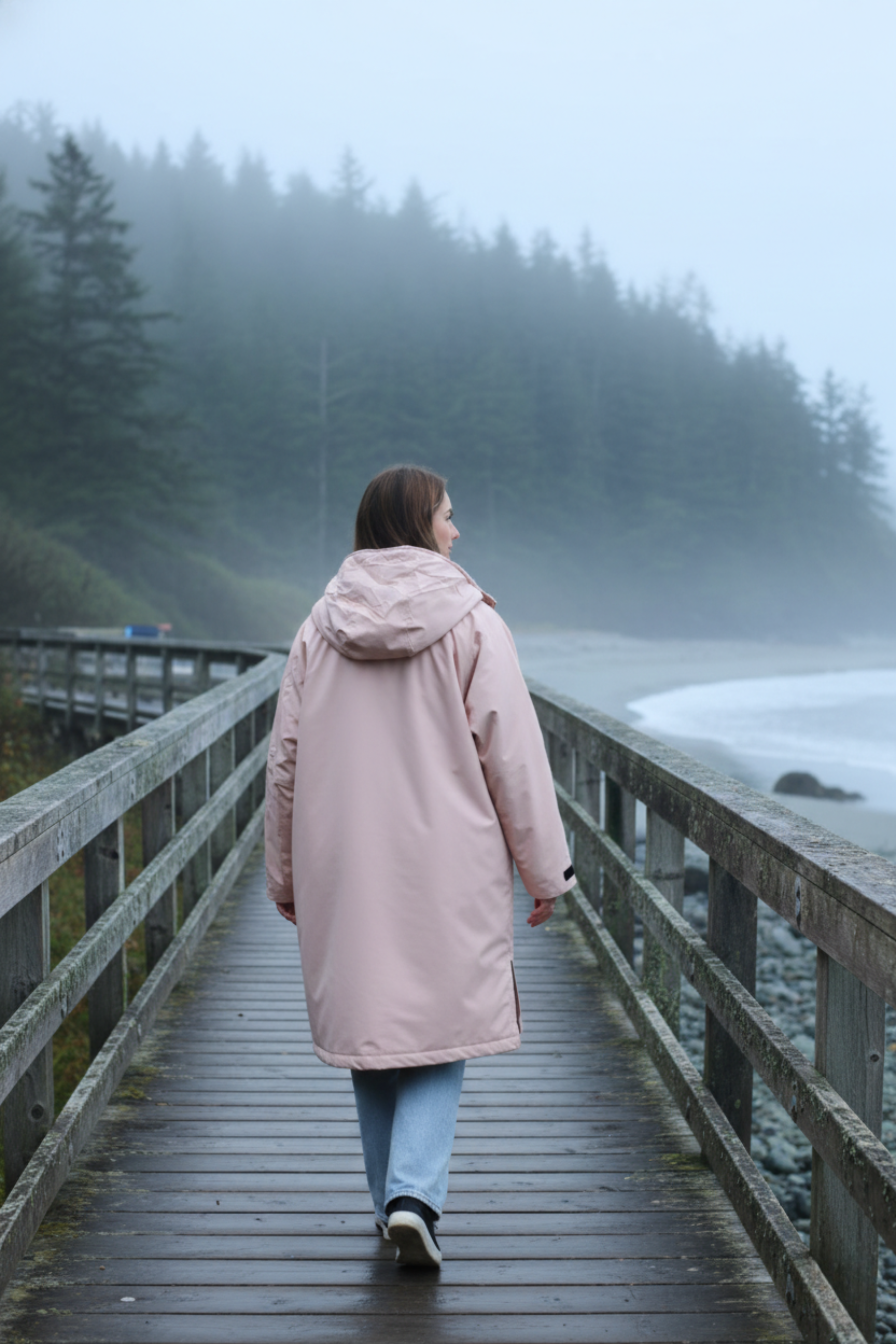 Person walking on a wooden bridge over a misty lake with trees in the background